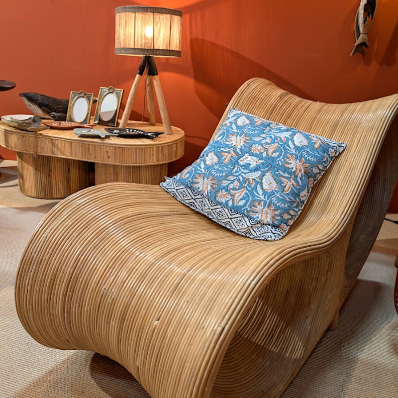 Présentation du coussin sur une chaise longue en rotin sous une lumière chaude.