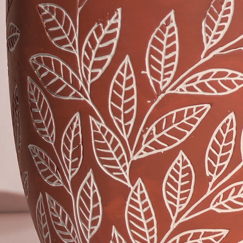 Détail macro du feuillage blanc en relief, gravé sur la céramique terracotta pour un rendu artisanal.