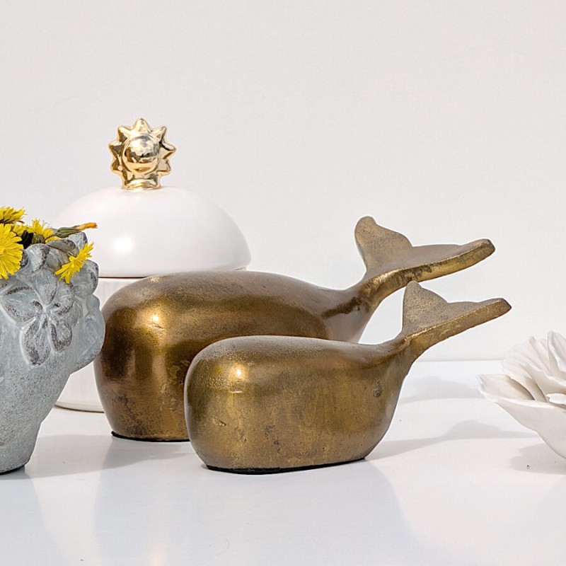 Mise en scène du duo de baleines dorées avec accessoires déco du catalogue Deco-Delight sur fond blanc épuré.