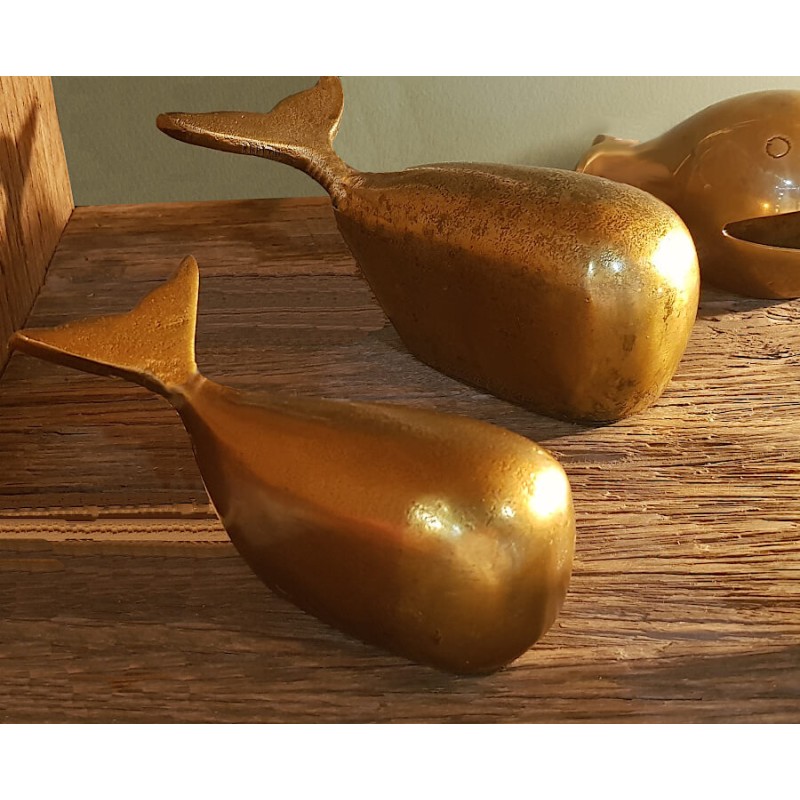 Les deux baleines décoratives sur une étagère en bois brut, avec une lumière mettant en valeur leur éclat doré.