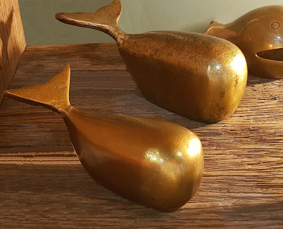 Les deux baleines décoratives sur une étagère en bois brut, avec une lumière mettant en valeur leur éclat doré.