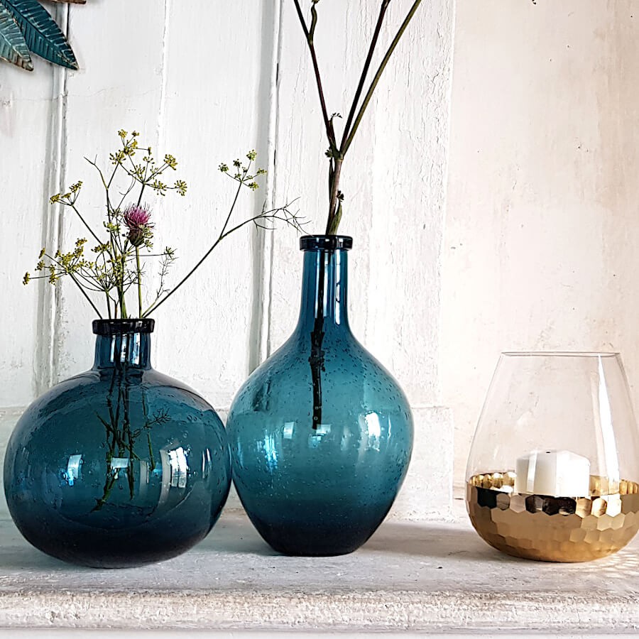 Vase en verre bullé bleu à côté du vase effilé et du photophore transparent et doré, sur une cheminée.