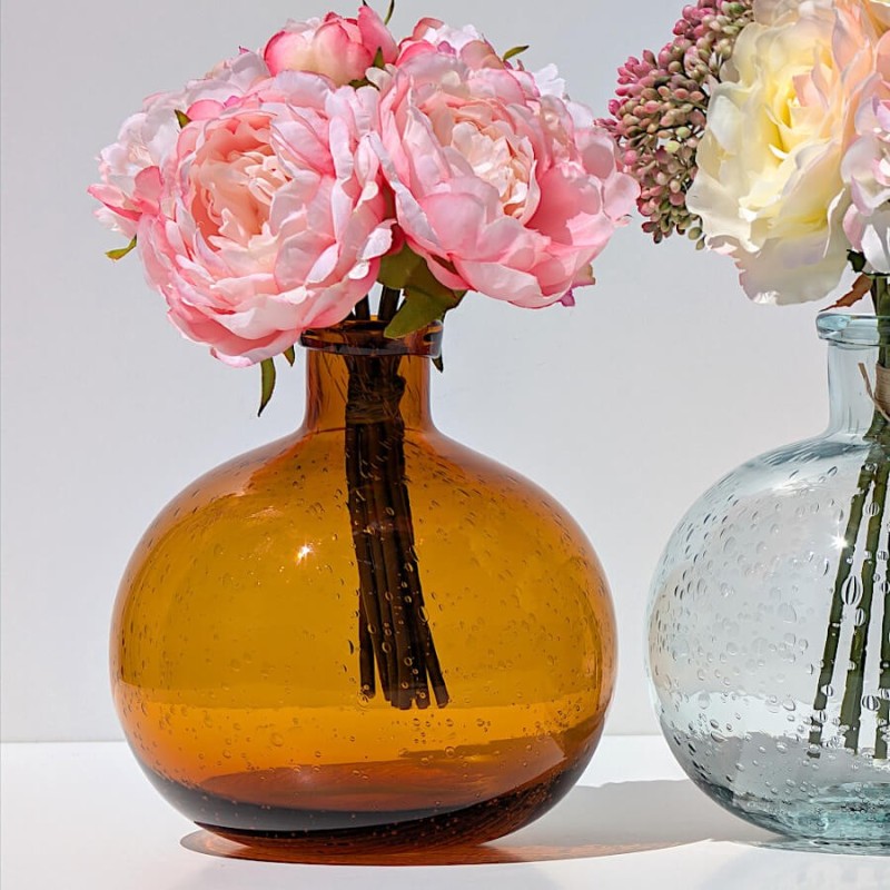 Le vase en verre bullé rouille aux reflets ambrés, avec un bouquet de roses artificielles pour un contraste chic.