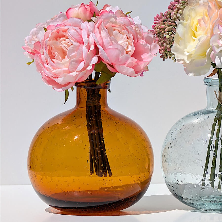 Le vase en verre bullé rouille aux reflets ambrés, avec un bouquet de roses artificielles pour un contraste chic.