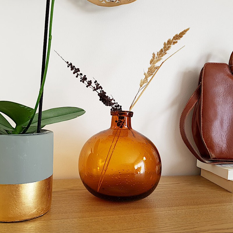 Mise en scène : le vase rouille avec une branche de fleurs séchées, à près du cache pot bicolore ciment et doré.