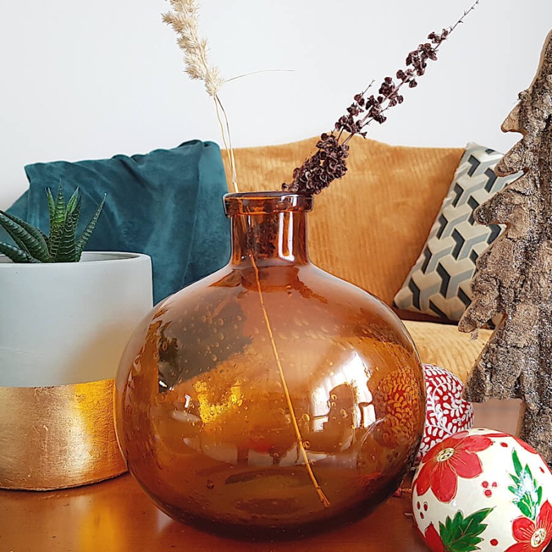 Vase en verre bullé teinte rouille près d'un cache pot ciment et or, sur une table de fête.