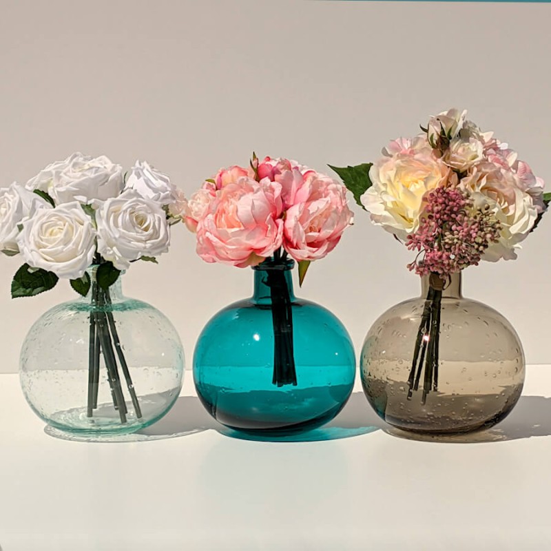 Le vase turquoise garni de fleurs élégantes, entre les vases en verre bullé vert d'eau et marron.