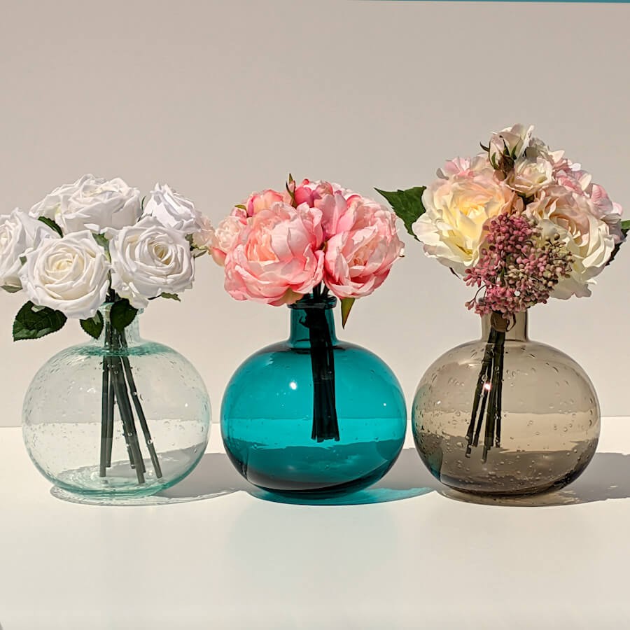 Le vase turquoise garni de fleurs élégantes, entre les vases en verre bullé vert d'eau et marron.