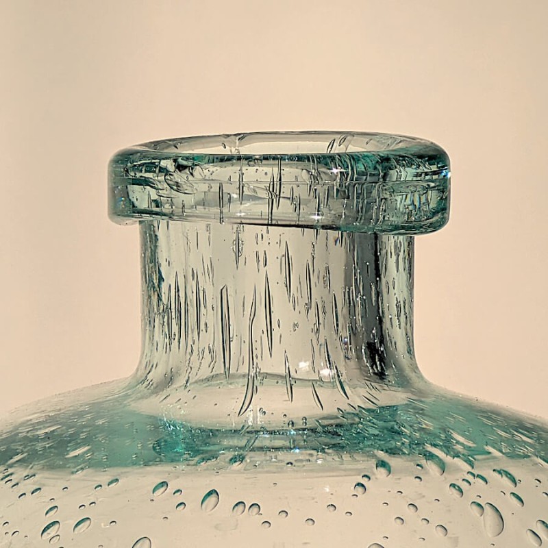 Zoom sur le col étroit et l'ouverture circulaire du vase vert d'eau, avec des bulles incrustées dans le verre.