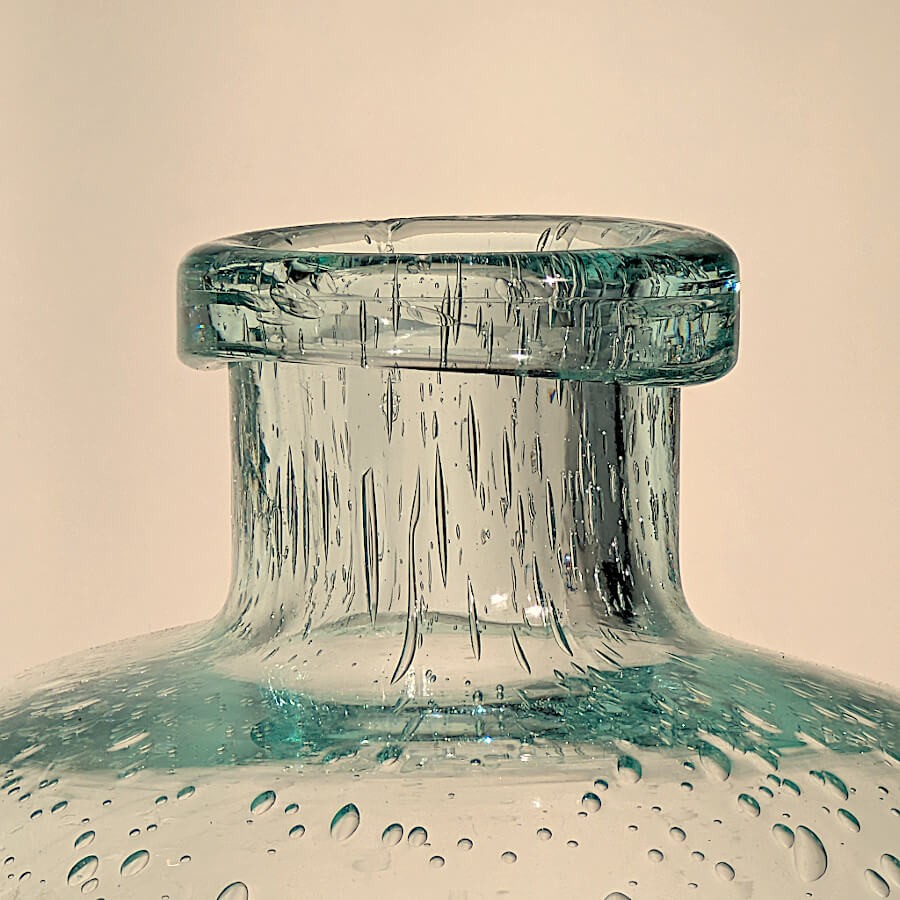Zoom sur le col étroit et l'ouverture circulaire du vase vert d'eau, avec des bulles incrustées dans le verre.