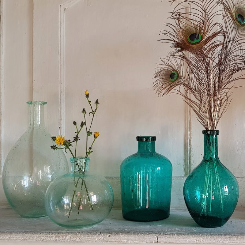 Fleurs séchées dans le vase en verre bullé vert d'eau, au milieu d'autres vases en verre bullé de différentes formes.