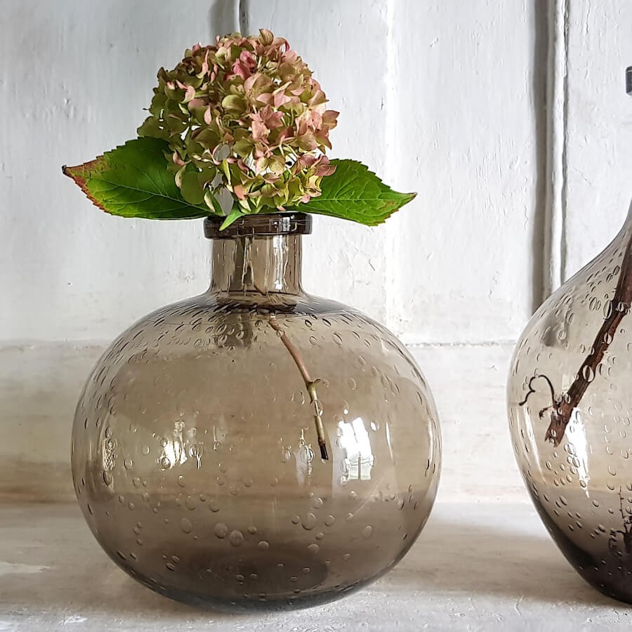 Le vase en verre bullé marron, portant une fleur d'hortensia, posé sur une cheminée.
