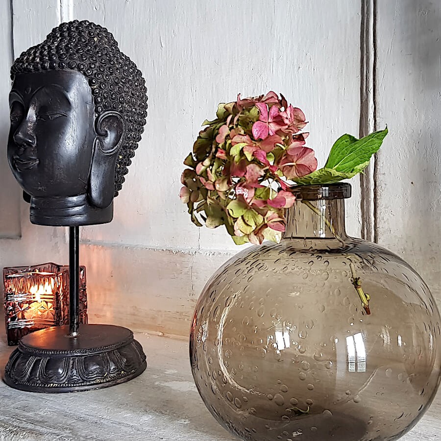 Mise en scène du vase en verre bullé marron dans une ambiance zen, avec une statue Tête de Bouddha (Deco-Delight).