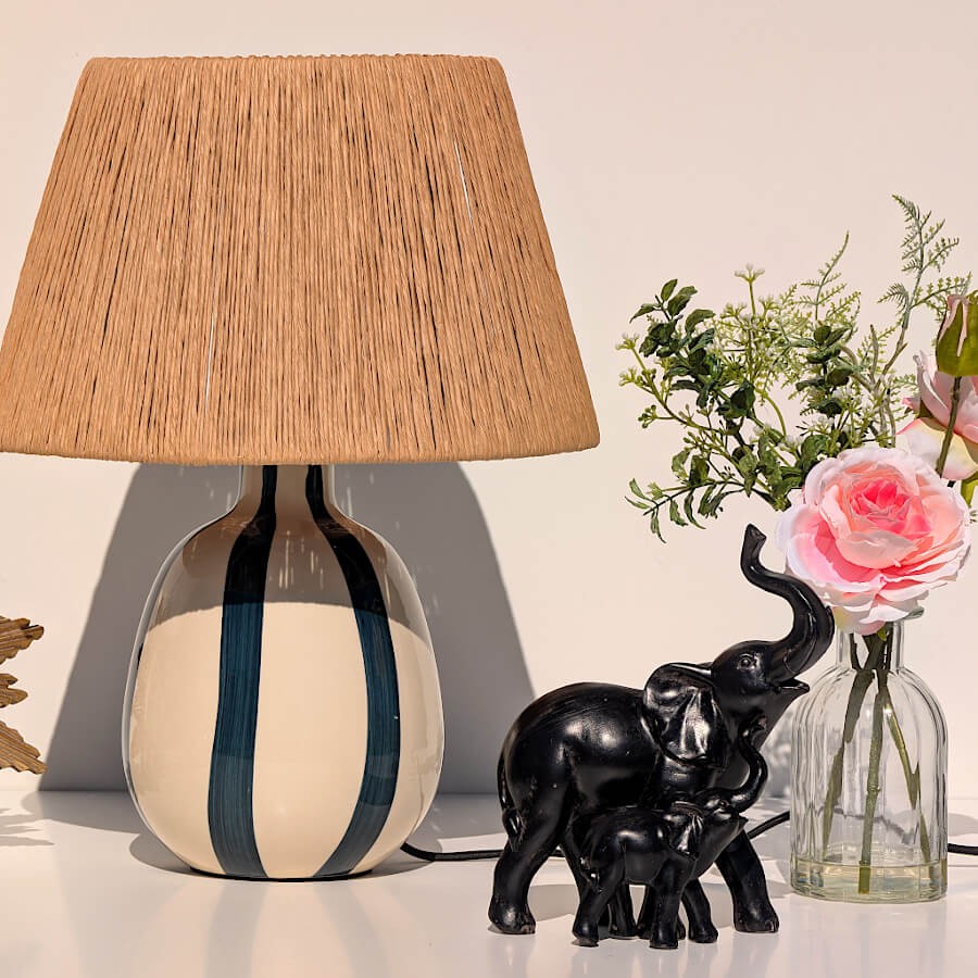Ambiance lumineuse : les éléphants posés près d'une lampe au pied rayé et abat-jour en jute.