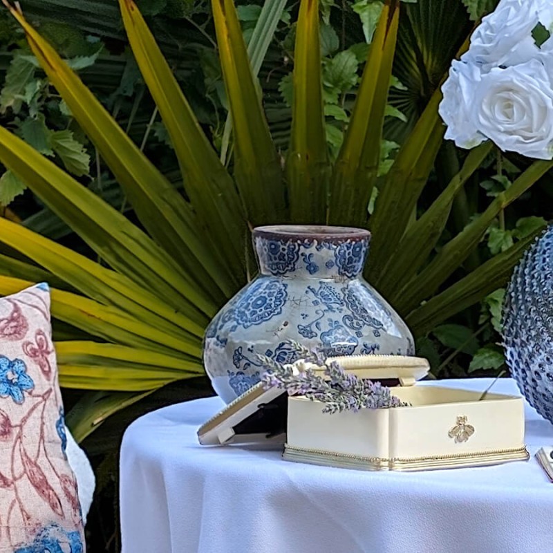 Jardin d'été : Le vase sur une table extérieure nappée de blanc, avec une boîte décorative et un coussin aux motifs coordonnés.