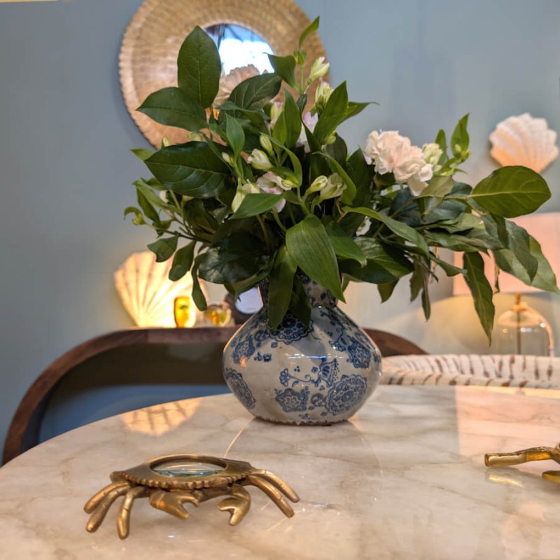 Vue d'ensemble du vase fleuri sur une table ronde, avec un miroir en rotin en arrière-plan.