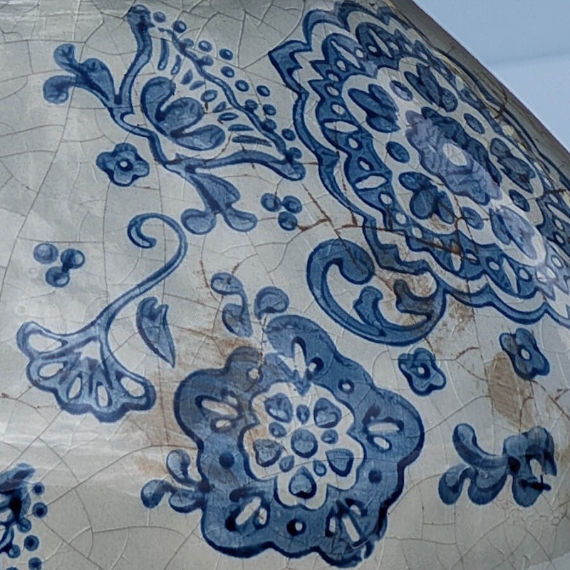 Focus motif : Détail d'une fleur bleue peinte avec ses arabesques, illustrant le style artisanal.