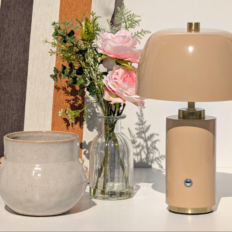 Le vase fleuri associé à une lampe nomade beige et un cache-pot en céramique beige moucheté.
