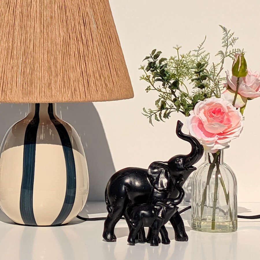 Mise en scène du vase avec la statuette éléphant noir et une lampe à abat-jour en fibres naturelles.