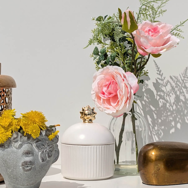 Jeu d'ombres : Le vase fleuri à côté d'un pot "visage" en céramique avec des ombres de feuilles projetées sur le mur.