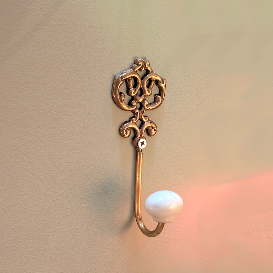 La patère fixée sur un mur beige, sublimée par un jeu d'ombres portée et un reflet lumineux rosé.
