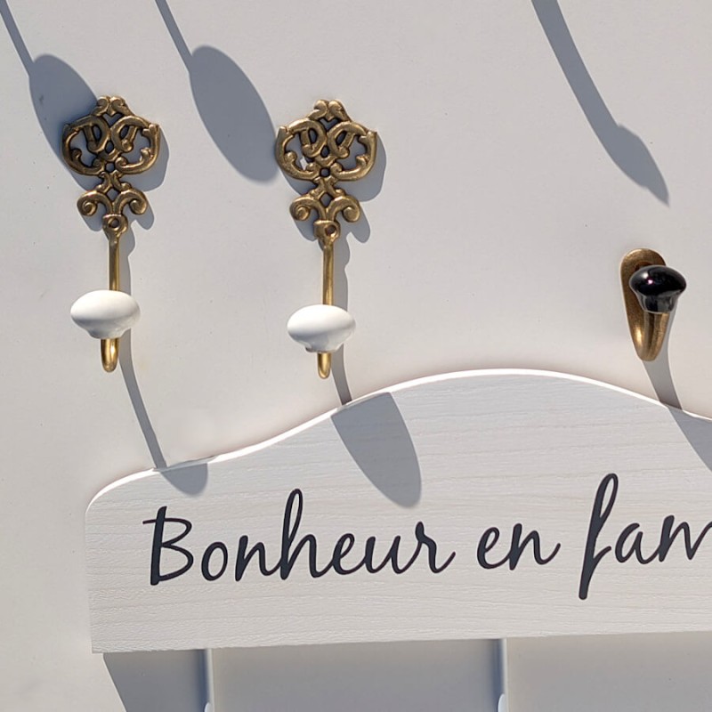 Un duo de patères dorées surmontant un modèle en bois blanc portant l'inscription décorative "Bonheur en famille".