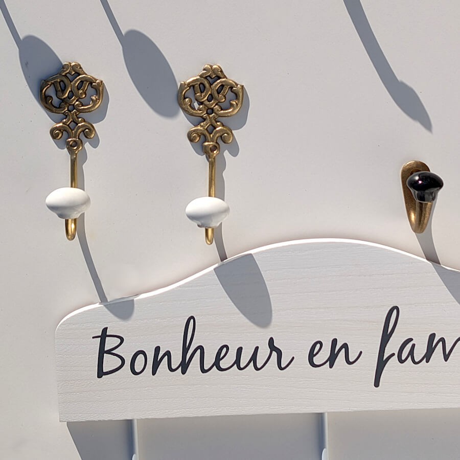Un duo de patères dorées surmontant un modèle en bois blanc portant l'inscription décorative "Bonheur en famille".