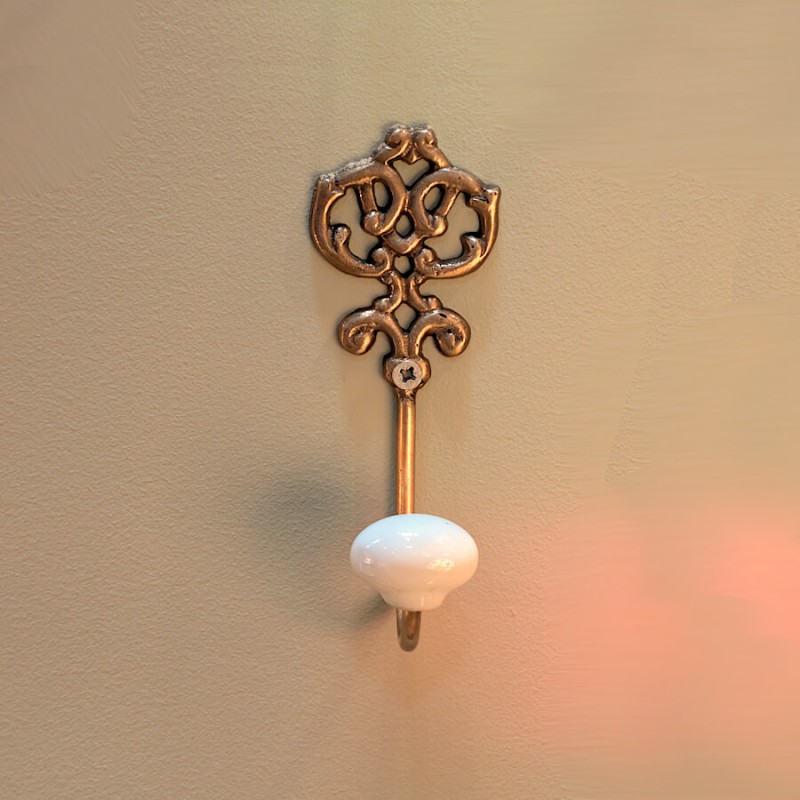 Vue frontale de la patère dorée sur mur beige, mettant en avant la douceur de l'éclairage latéral.