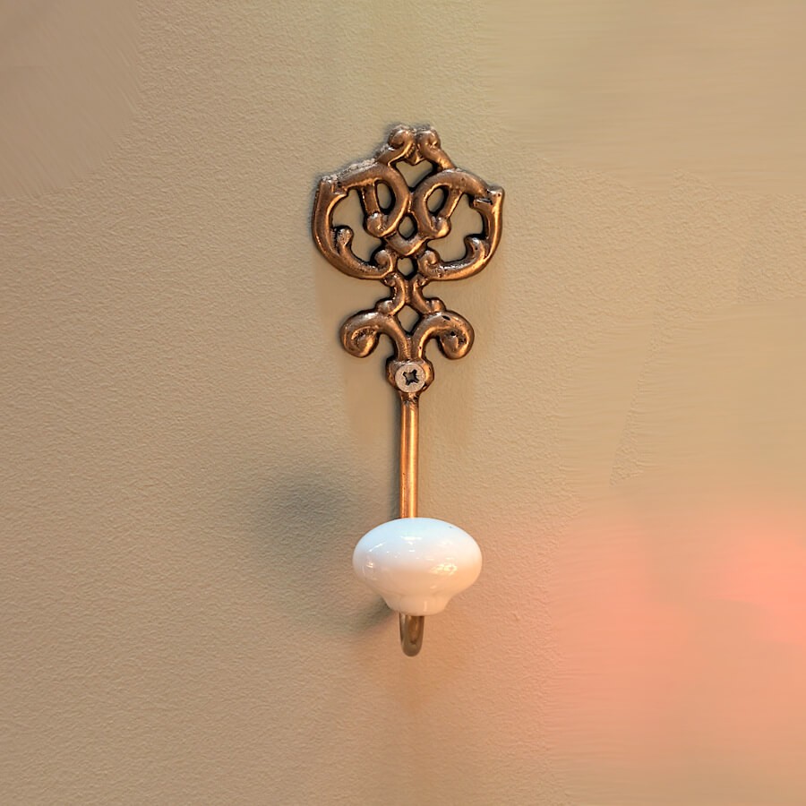 Vue frontale de la patère dorée sur mur beige, mettant en avant la douceur de l'éclairage latéral.