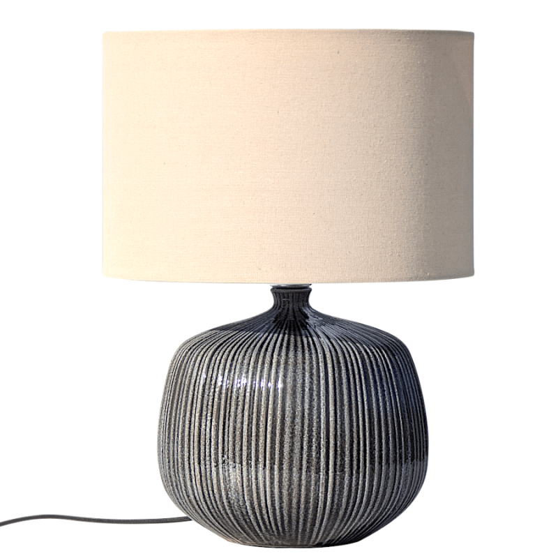 Lampe à poser avec pied arrondi en grès gris rainuré et abat-jour cylindrique en lin crème sur fond blanc.