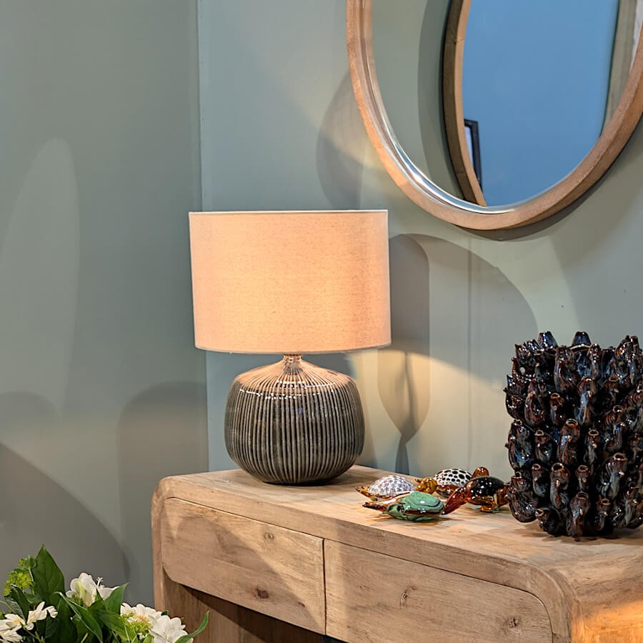 La lampe allumée posée sur une console en bois clair dans un intérieur contemporain aux tonalités douces.