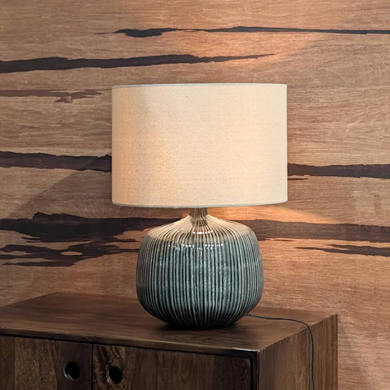 La lampe disposée sur un buffet en bois foncé, diffusant une lumière chaleureuse contre un mur texturé.
