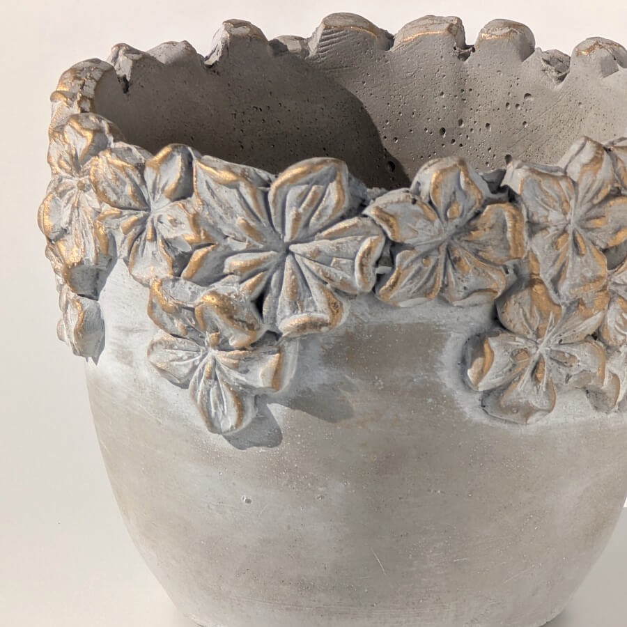 Zoom relief : Détail des fleurs sculptées et de la patine dorée sur ciment.