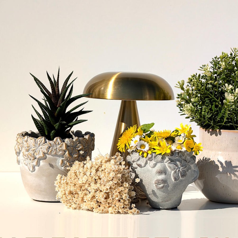 Le cache-pot associé à une lampe de table dorée et d'autres céramiques fleuries sous un soleil radieux.