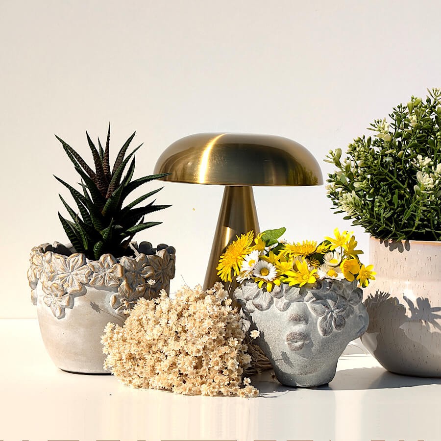 Le cache-pot associé à une lampe de table dorée et d'autres céramiques fleuries sous un soleil radieux.