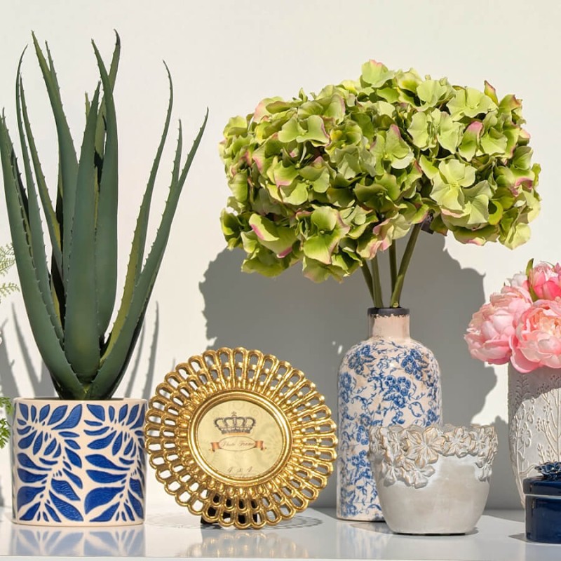 Scène déco estivale réunissant le cache-pot, une plante succulente, le cadre doré ajouré et le grand vase bleu et blanc.