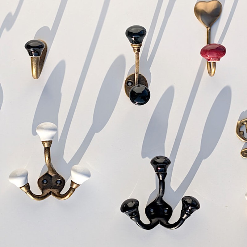 Mise en scène murale : Patères rétro en céramique noire et modèles Deco-Delight en faïence blanche alignés.