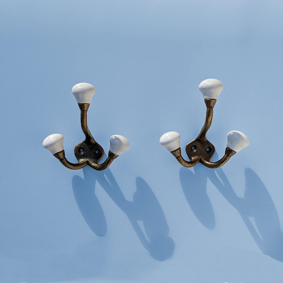 Duo en situation : Deux patères dorées et blanches fixées côte à côte sur un mur bleu ciel.