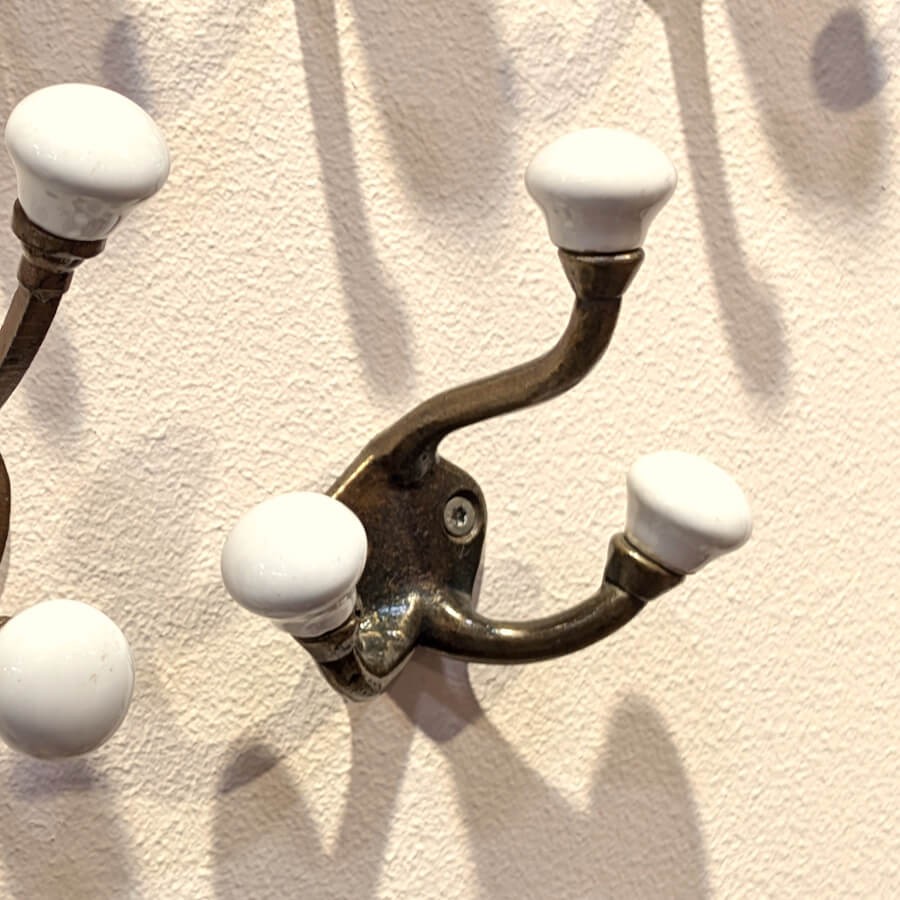 Jeu d'ombres : Patère d'entrée dorée fixée sur un mur blanc avec une ombre portée graphique.