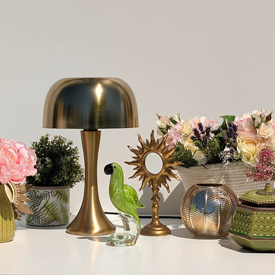 Mise en scène précieuse : Photophore doré scintillant à côté d'une lampe champignon laiton et d'un perroquet en verre.