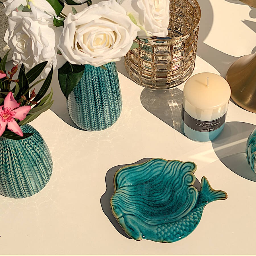 Coupelle sirène turquoise disposée sur une table près de roses blanches et de la bougie Nuances aquatiques Deco-Delight.