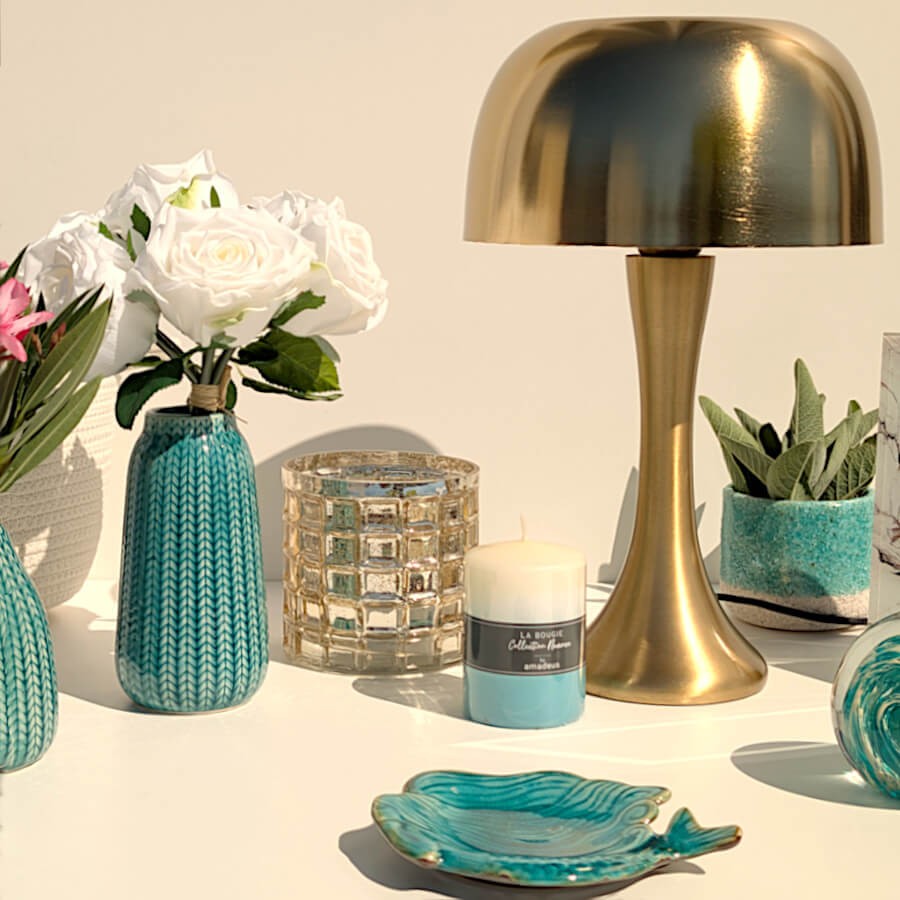 Vue de situation épurée : Plat sirène en grès à côté d'un vase strié bleu et d'une lampe dorée.