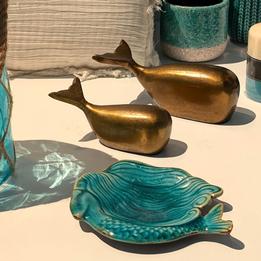 Vide-poches en céramique turquoise devant deux statuettes de baleine en métal doré, collection Deco-Delight.