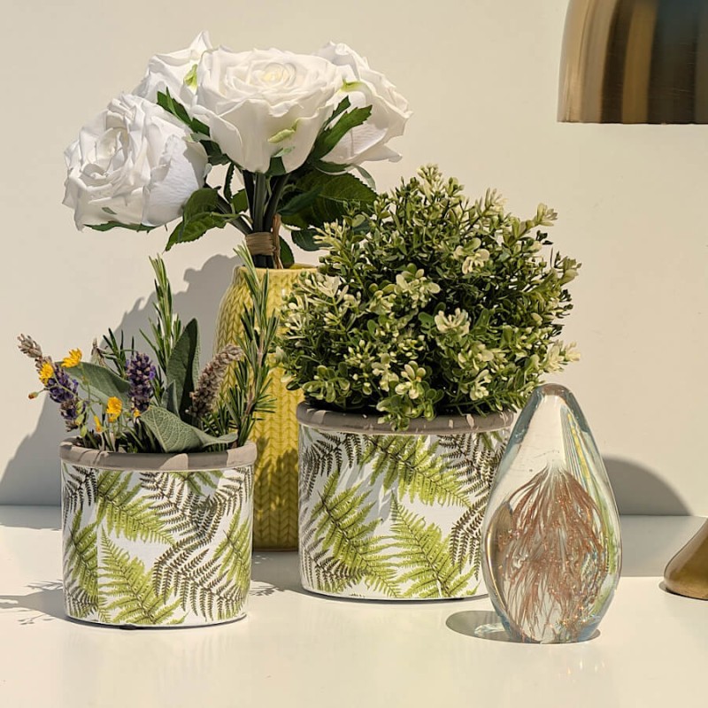 Mise en scène lumineuse : Petit pot en ciment végétal à côté d'un presse-papier en verre et de roses blanches.
