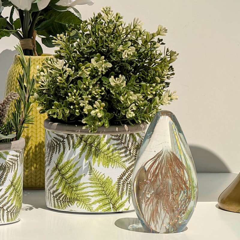 Vue de situation lumineuse : Pot en ciment au motif végétal à côté d'un presse-papier en verre et de plantes.