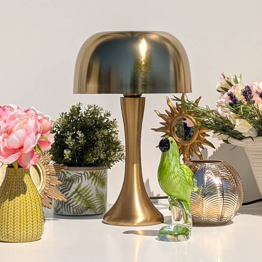 Mise en scène chic : Pot en ciment fougère près d'une lampe dorée champignon et d'un perroquet de la collection.