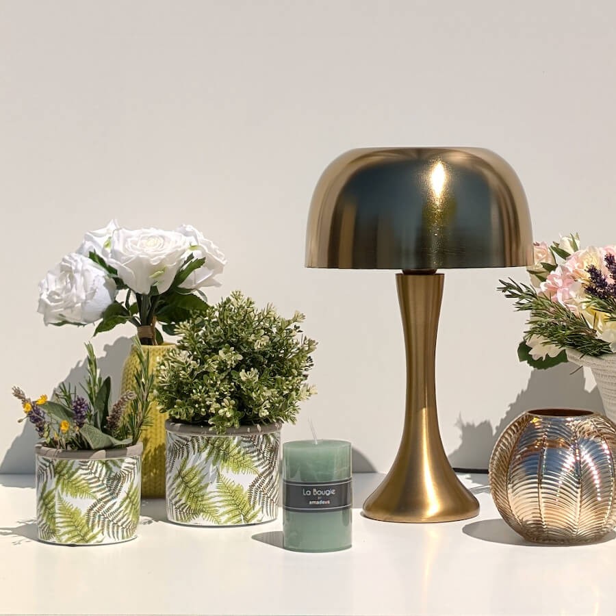 Vue d'ensemble épurée : Pot fougère en ciment à côté d'une bougie verte et d'une lampe de table dorée.