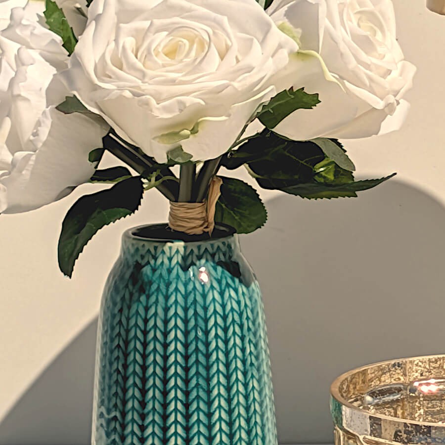 Focus col du vase : Vue rapprochée sur le bouquet de roses blanches disposé dans le vase turquoise.
