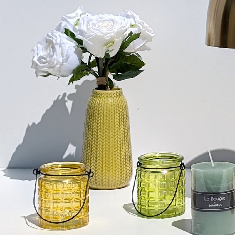 Mise en scène avec le vase fleuri de roses blanches, près de photophores en verre et bougie pilier vert amande.