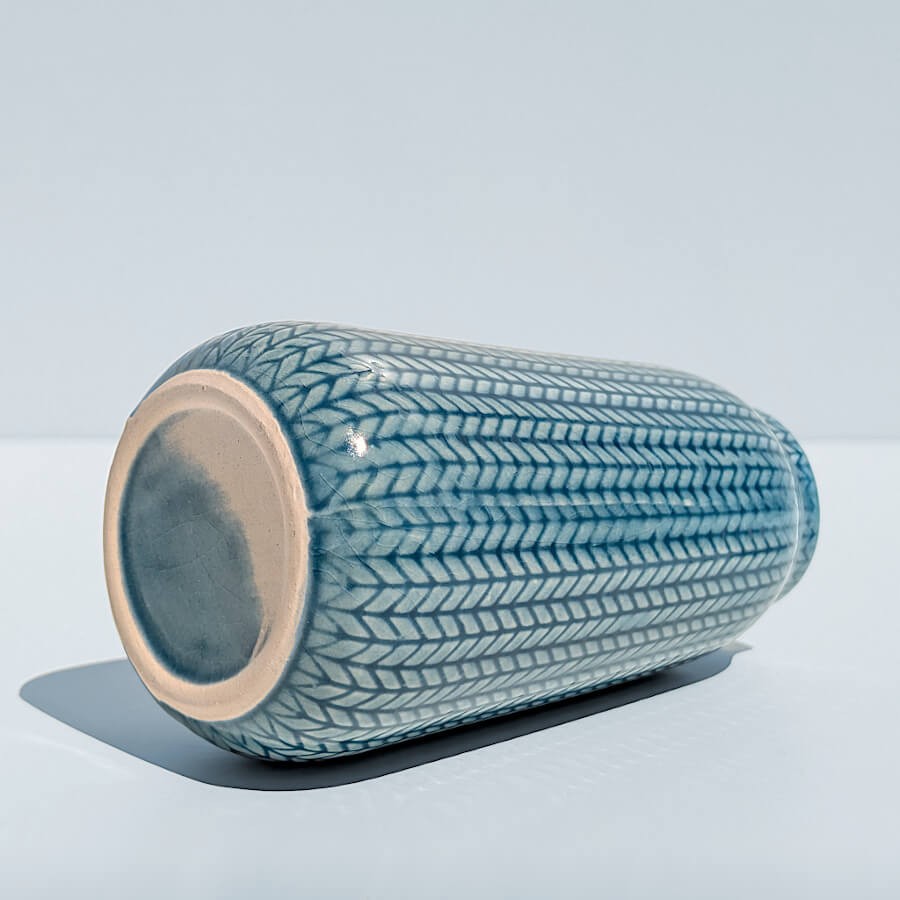 Vue couchée : Vase épi bleu allongé montrant son émaillage intégral et son fond beige.